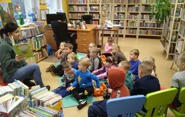 Dzieci siedzą na karimatach w bibliotece w Zblewie,a bibliotekarka czyta bajkę.