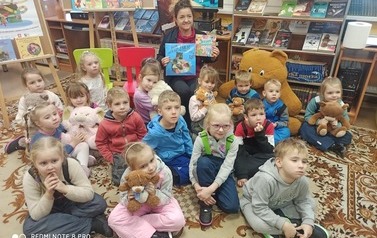 Zdjęcie grupowe przedszkolak&oacute;w w bibliotece. Bibliotekarka trzyma książke o misiach.