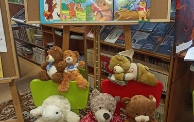 Tablica kurkowa przystrojona w grafiki o misiach i książeczki o misiach. Na krzesełkach niżej siedzą misie.