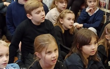 Dzieci siedzą na dywanie i oglądają teatrzyk.