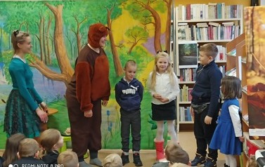 Czw&oacute;rka dzieci stoi przy misiu i dziewczynie. Widoczna publiczność dziecięca.