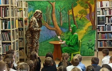 Przebrana żaba siedzi przy stoliku, a przy niej stoi tygrysek i rozmawiają.