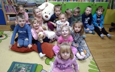 Dzieci siedzą w grupie na dywanie z białym dużym miesiem po środku.