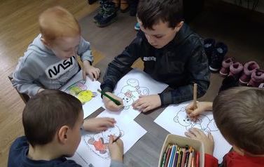 Czterech chłopc&oacute;w siedzi przy stoliku i koloruje misie.