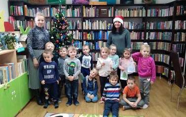 Zdjęcie grupowe przy choince dzieci z Panią nauczycielką i Bibliotekarką w czapce świetego Mikołaja.