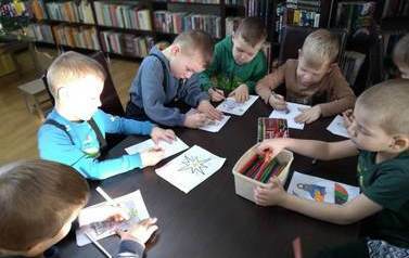 Chłopcy siedzą przy stole i kolorują obrazki z motywem świątecznym.
