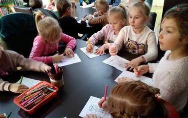 Dzieci siedzą przy stolikach i i kolorują obrazki z motywem świątecznym