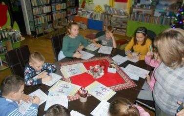 Dzieci siedzą przy stole i uzupełniają świąteczne karty pracy.