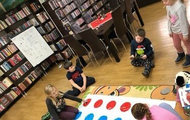 Pięcioro dzieci gra w grę rozłożoną na dywanie o nazwie TWISTER