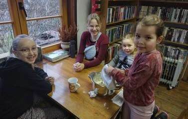 Jedna dziewczynka miksuje mikserem ciasto do gofr&oacute;w, a trzy dziewczynki siedzą obok i  patrzą uśmiechając się. 