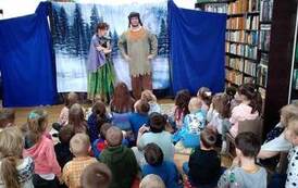 Aktorzy stoją w tle zaśnieżonego lasu. Publiczność dziecięca patrzy.