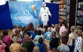 Na tle zaśnieżonego zamku stoi Elza i Bałwan Olaf rozmawiając. Publiczność dziecięca patrzy.