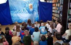 Na tle zaśnieżonego zamku stoi Elza. Dzieci z zaciekawieniem patrzą.