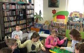 Sz&oacute;stka dzieci siedzi przy stole i gra w piłkarzyki. Za stołem stoi chłopiec i patrzy w aparat.