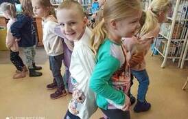 Dziewczynka z chłopcem ustawieni do siebie plecami i ze złączonymi rękoma. W tle widać inne pary.