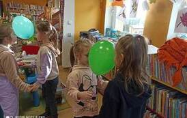 Dwie pary tańczących dziewczynek trzymających się za ręce twarzą do siebie i głowami trzymając zielone baloniki.