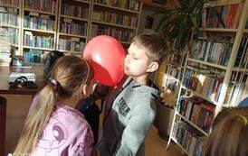 Chłopiec z dziewczynką stoją w parze twarzą do siebie trzymając się za ręce i głowami trzymjąc czerwony balon.