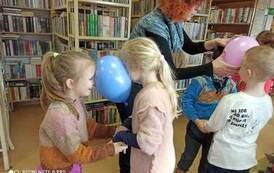 Dwie pary dzieci tańczące parami i trzymające glowami wsp&oacute;lnie balonik. Nauczycielka pomaga jednej parze przytrzymać balonik.