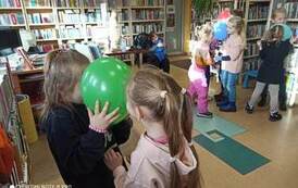 Dzieci tańczą w parach trzymając się za ręce, głowami trzymając wsp&oacute;lnie balonik.