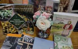 Na stoliku wyłożone książki regionalne z widocznymi tytułami. Po środku nich stoi wazonik ze sztucznymi kwiatami.