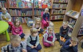 Dzieci siedzą w rozsypce na poduszkach i słuchają czytanej bajki