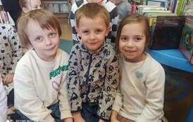 Z przodu siedzą dw&oacute;ch chłopc&oacute;w i jedna dziewczynka po prawej stronie. W tle widać inne dzieci.