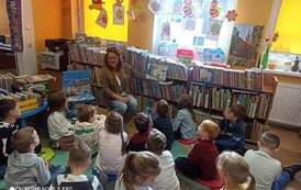 Dzieci siedzą na karimatach,a bibliotekarka czyta im bajkę pokazując przy tym ilustracje.