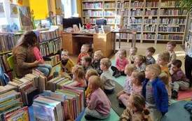 Dzieci siedzą na karimatach,a bibliotekarka pokazuje im r&oacute;żowe siedzisko z numerem 8.