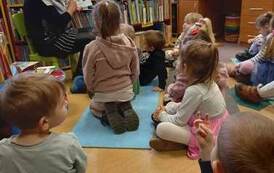 Dzieci siedzą na karimatach,a bibliotekarka czyta im bajkę pokazując ilustracje.