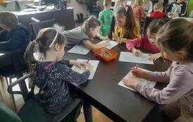 Dzieci siedzą przy stołach i kolorują obrazki przedstawiające postaci z baśni Andresrena.