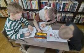 Trzech chłopc&oacute;w siedzi przy małym stoliku i kolorują obrazki z postaciami z baśni Andresena