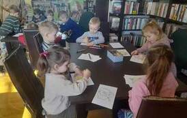 Dzieci siedzą przy stołach i kolorują obrazki przedstawiające postaci z baśni Andresrena.