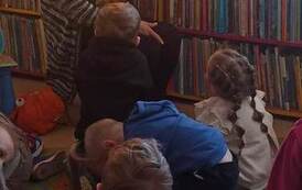 Dzieci siedzą na dywanie i słuchają bajki o zajączku wielkanocnym, kt&oacute;rą czyta im bibliotekarka.