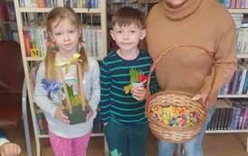 Bibliotekarka ze Zblewa stoi z dw&oacute;jką dzieci trzymając koszyk z cukierkami.