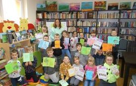 Dzieci stoją w grupie ze swoją nauczycielką trzymając w ręce swoje prace na kartkach.