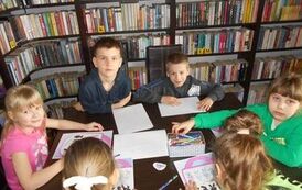 Dzieci siedzą przy stole i wykonują świąteczne zadania na kartkach.