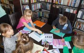 Dzieci siedzą przy stole i wykonują świąteczne zadania na kartkach. 