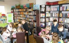 Dzieci siedzą przy dw&oacute;ch stołach i wykonują świąteczne zadania na kartkach.