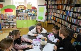 Dzieci siedzą przy stole i wykonują zadania na kartkach o kr&oacute;liczkach.