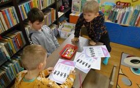 Trzech chłopc&oacute;w siedzi przy stoliku i rozwiązuje zadania na kartkach o kr&oacute;liczkach.