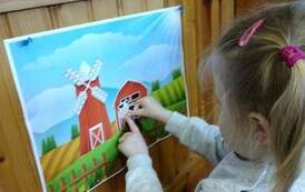 Na drzwiach jest przyczepiony plakat na kt&oacute;rym jest farma i dziewczynka przykleja na nim zwierzątko.