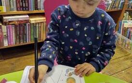 Dziewczynka stoi przy stoliku i na kartce rysując łączy zwierzątka z ich domkami. 