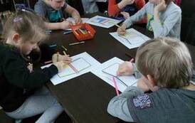 Dzieci siedzą przy stołach i na kartkach projektują okładkę do książki.