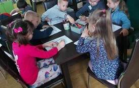 Dzieci siedzą przy stole i na kartkach projektują okładkę do książki.