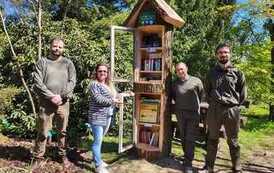 Przy nowo postawionej biblioteczce w Arboretum w Wirtach stoją Kierownik Gminnej Bilbioteki w Zblewie: Emilia Bielska i trzej leśnicy. Biblioteczka jest zrobiona z drewna w kształcie wieży z oszklonymi p&oacute;łeczkami.