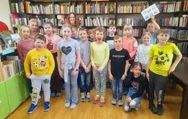 Zdjęcie grupowe dzieci i ich Pani przy p&oacute;łkach z książkami.