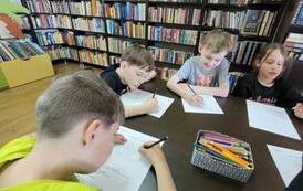 Chłopcy przy stole rozwiązują krzyż&oacute;wkę, na stole leżą kredki.