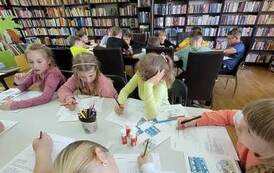 Dzieci siedzą przy stołach i rozwiązują krzyż&oacute;wkę, na stole są kleje i poprzednie prace zrobione przez dzieci.