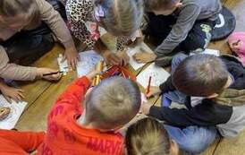 Dzieci siedzą na podłodze i kolorują obrazki.