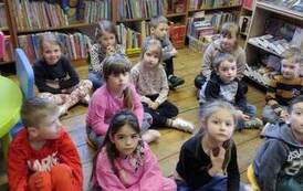Dzieci siedzą na siedziskach i słuchają co m&oacute;wi bibliotekarz.